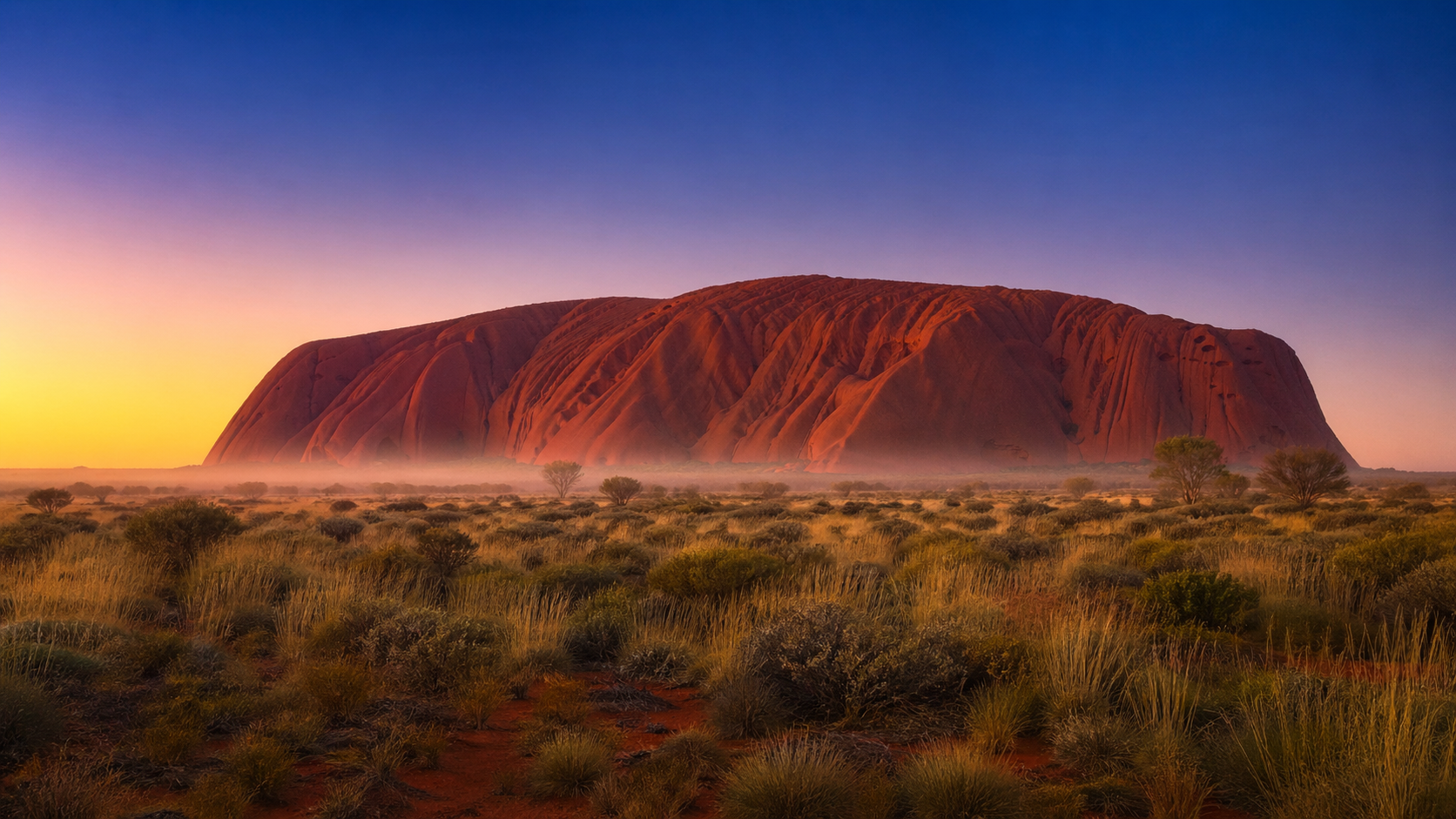 Uluru au lever du soleil dans le Red Centre australien, roche rouge baignée de lumière dorée sous un ciel clair
